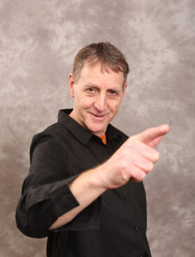 Mann in schwarzem Hemd zeigt mit ausgestrecktem Finger vor grauem Hintergrund