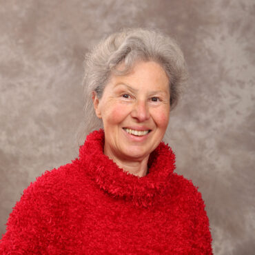 Ältere Frau mit grauen Haaren trägt roten Pullover vor neutralem Hintergrund