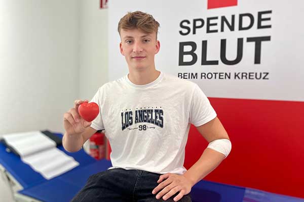 Person mit T-Shirt Los Angeles 98 hält rotes Herz vor Schild Spende Blut beim Roten Kreuz