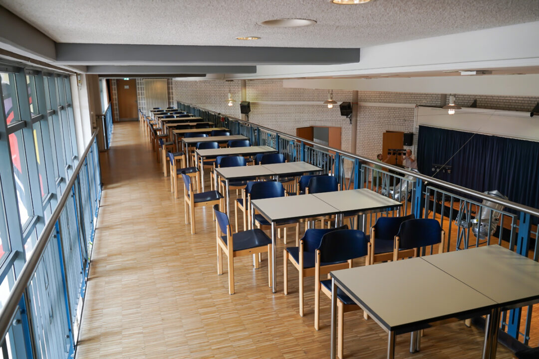 Obere Galerie mit Reihen aus Tischen und Stühlen entlang großer Fenster, Blick zur Bühne rechts