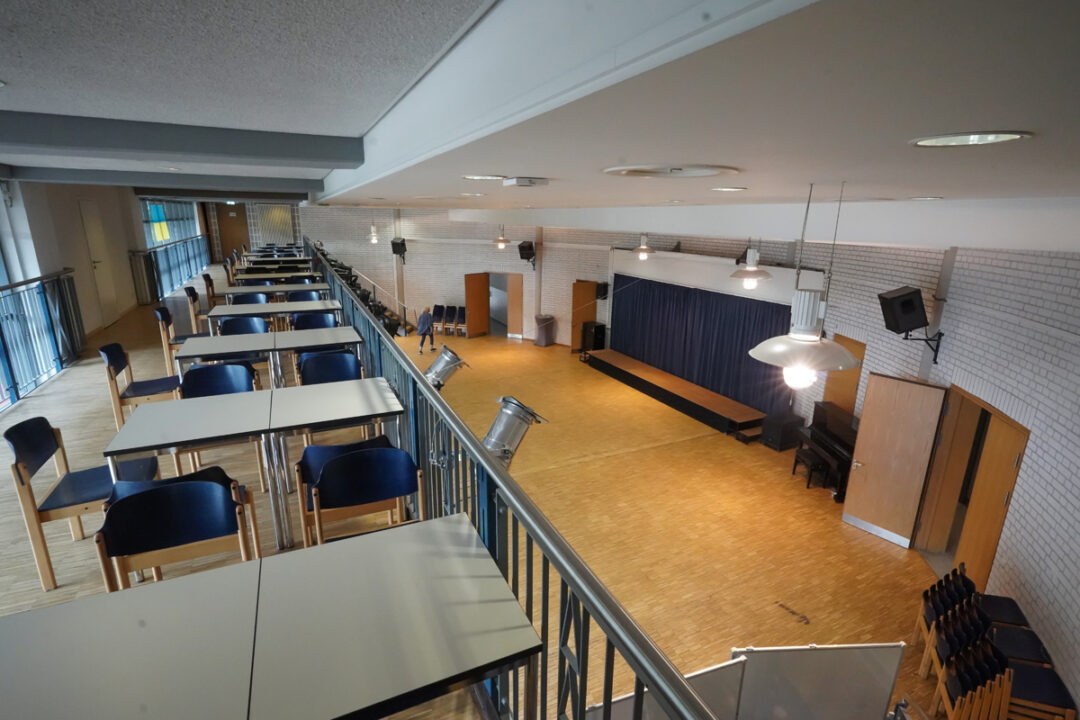 Blick von Galerie auf großen Saal mit Bühne, Vorhang, Klavier und freier Parkettfläche