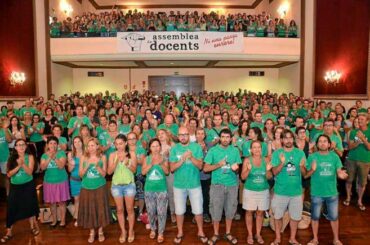 Große Gruppe von Menschen in grünen Shirts in einem Saal, Banner mit Text auf Balkon 