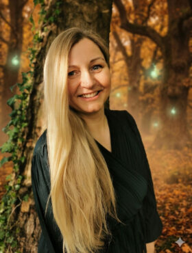 Person mit langen blonden Haaren in schwarzer Kleidung vor herbstlichem Waldhintergrund